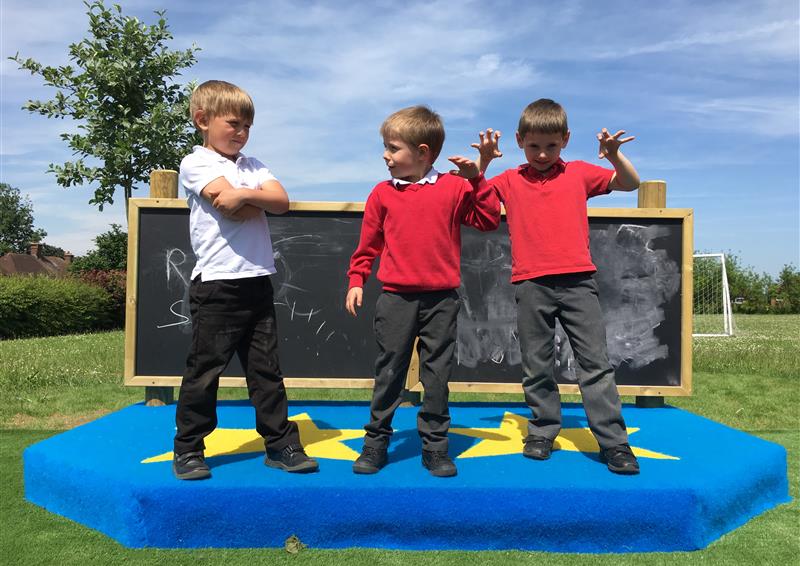 3 young boys playing on our performance stage, a giant chalk board which is part of the performance stage is in the background behind the boys.