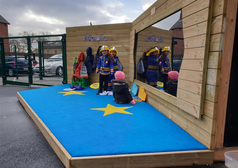 two children dressed up as firefighters on our performance stage, another girl is sat on the floor of the stage looking in the mirror.
