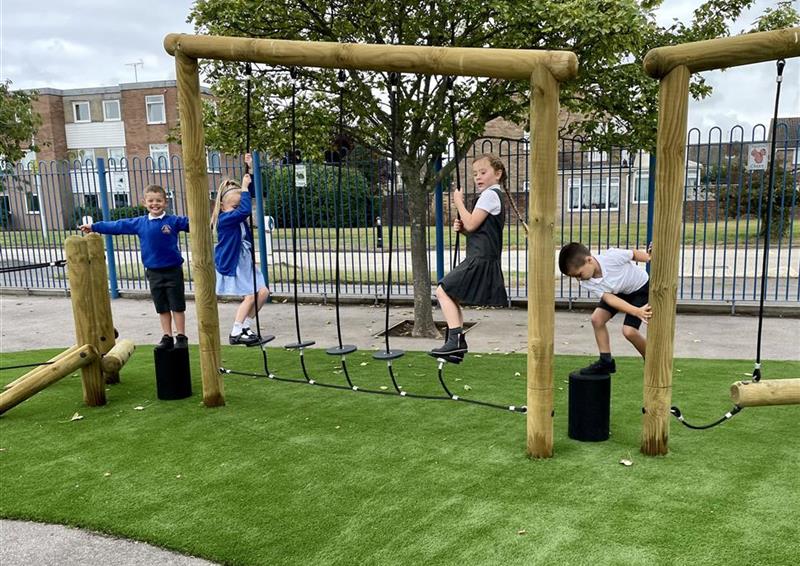 4 children playing on the trim trail, 2 young girls are playing on the stepping stone transverse and the 2 young boys are playing on the side. A layer of artificial grass has been placed underneath the Trim Trail.