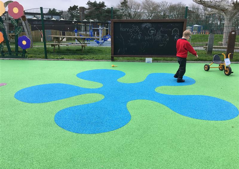 a blue wetpour splash amid green artificial grass surfacing being played on by pupils at a primary school