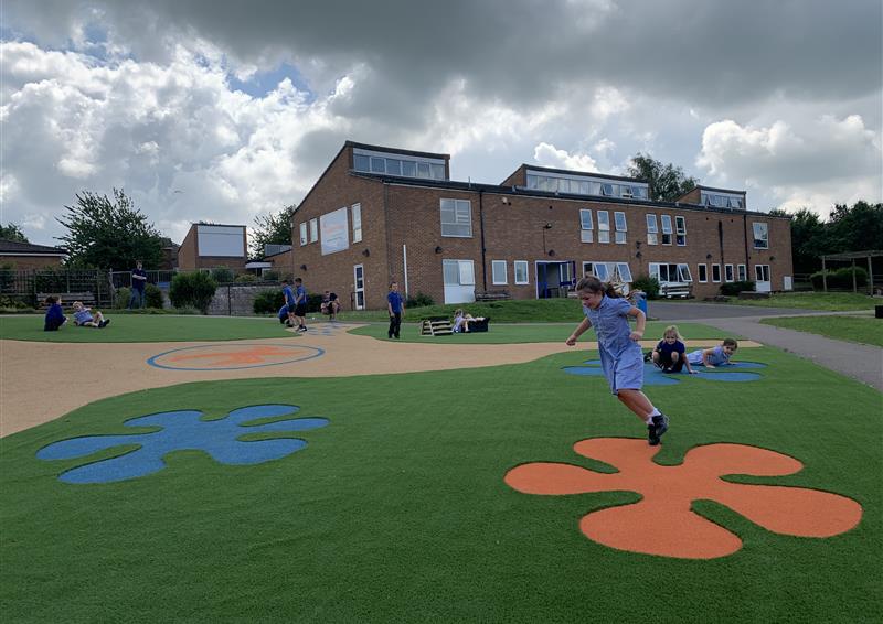 orange and blue wetpour splashes on green artificial grass surfacing as a child in blue school uniform sits on one of the splashes