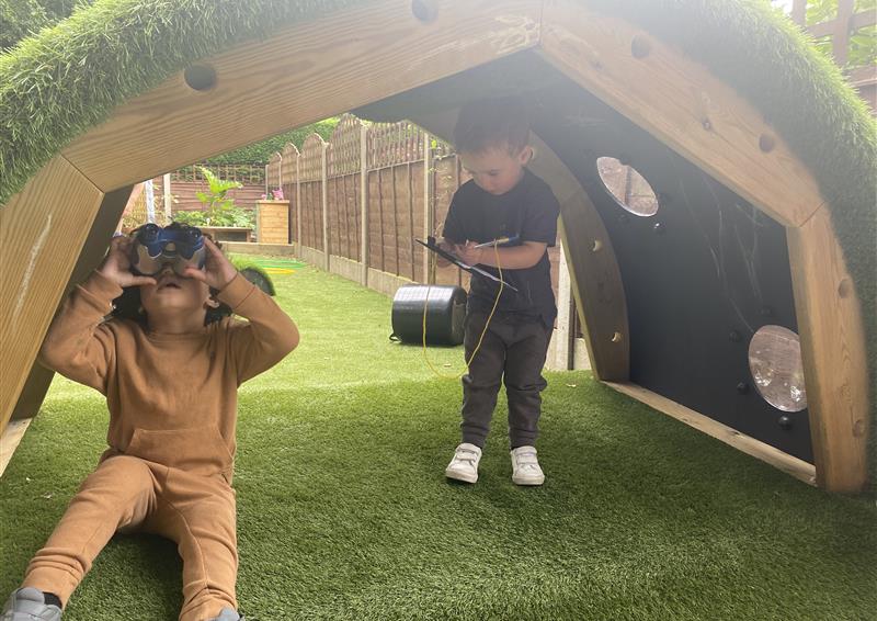 2 children sat underneath the hill den, one young boy is looking through binoculars looking out the bubble window.