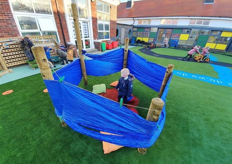 3 children playing under their den making posts, there is a cloth on top to act as sheler
