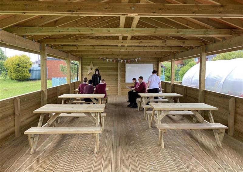 5 children sat on benches under their gable end, they are doing a lesson on the whiteboard at the front. 