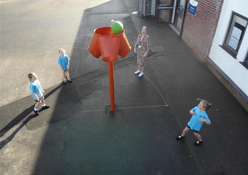 4 children and one teacher throwing balls into the red 4 way ball shoot in their playground
