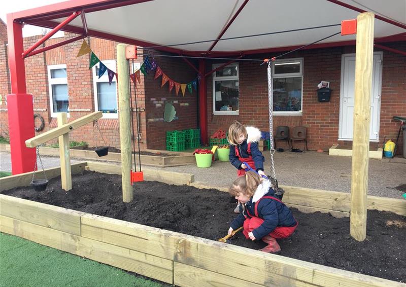 2 children paynig in the dig pit at their school, they are using the rope and pulley device on the dig pit to distribute the mud across.