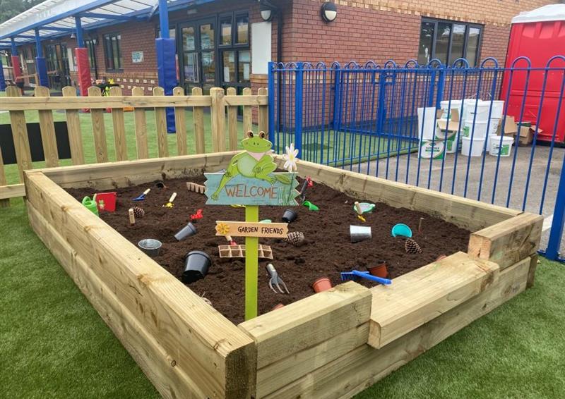 A picture of an allotment that was installed at milton primary school, there is mud filled into the allotment with spades and buckets placed on top.