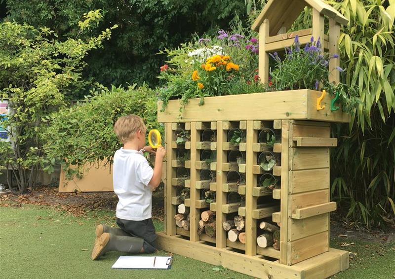 one young boy looking into the bug hotel with a magnifying glass