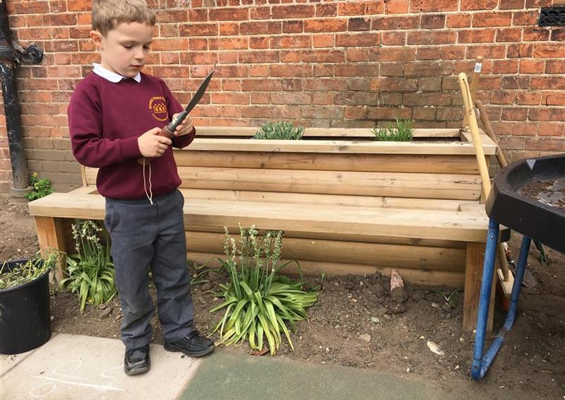 one young boy standing in front of the planter bench which has plants and flowers growing from it!