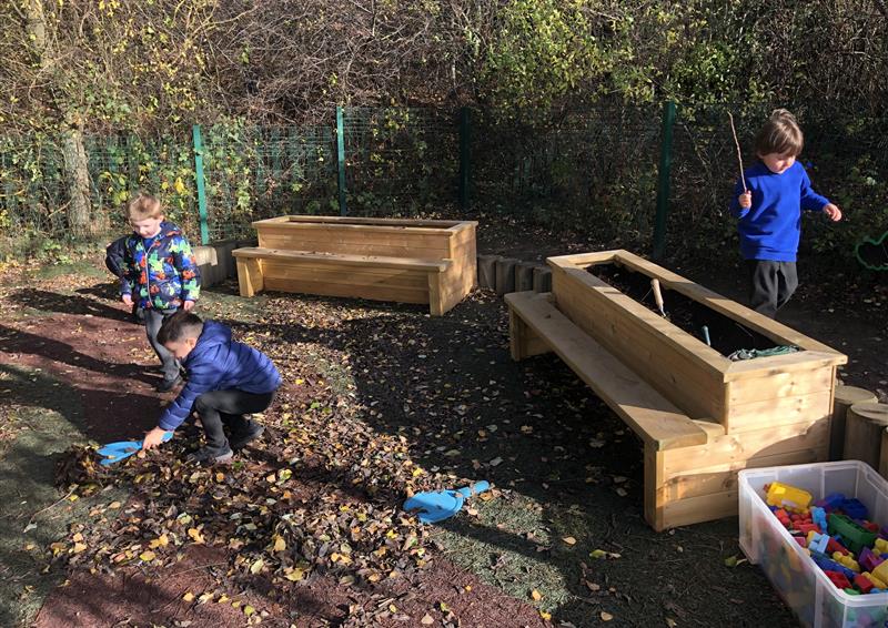 3 children playing outside in the mud with the planter benches behind them.