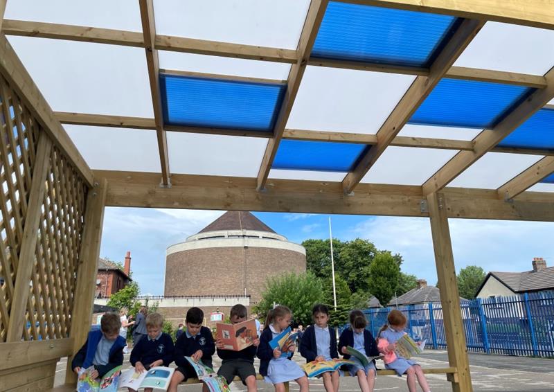 a photo showing pupils sat reading underneath a timber canopy with white and blue polycarbonate roof tiles