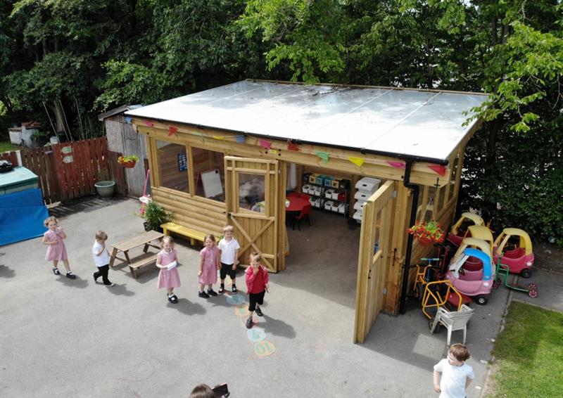 a birdseye view of a playground showing a timber canopy with sides and windows and double doors whilst children wait on the playground just outside