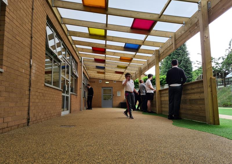 a timber canopy with beige wetpour  and colourful roof panels in orange, yellow, blue and red