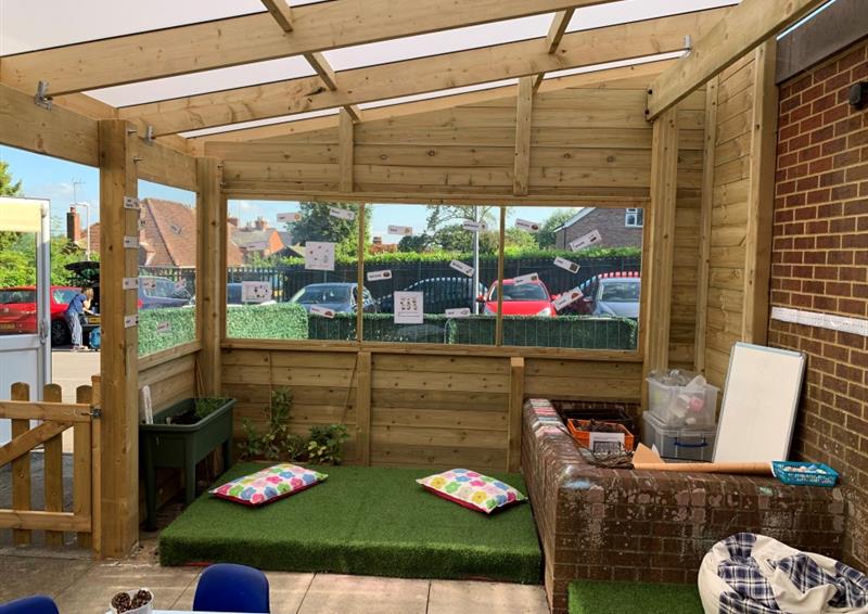 a canopy with grass surfacing inside and windows looking out onto the car park from the classroom
