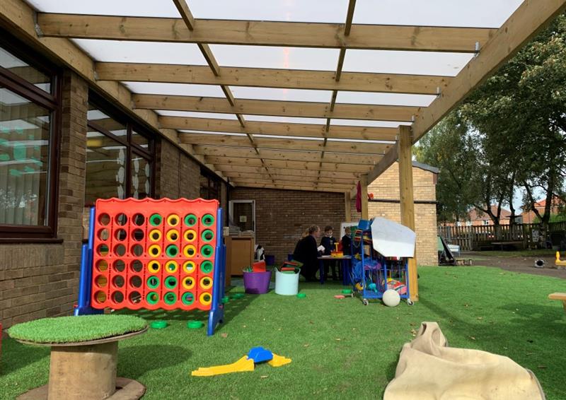 a timber canopy with white polycarbonate roof panels and artificial grass surfacing