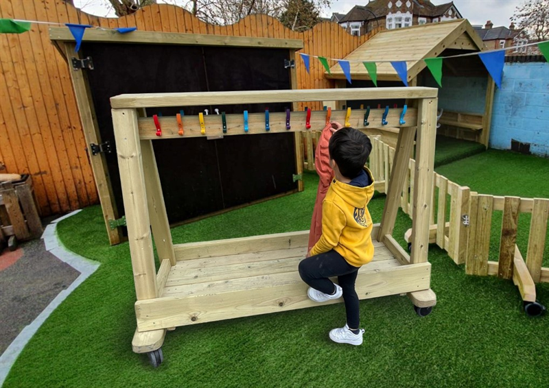a little boy in a yellow jumper hanging his coat onto one of the colourful coat hooks on the timber rack