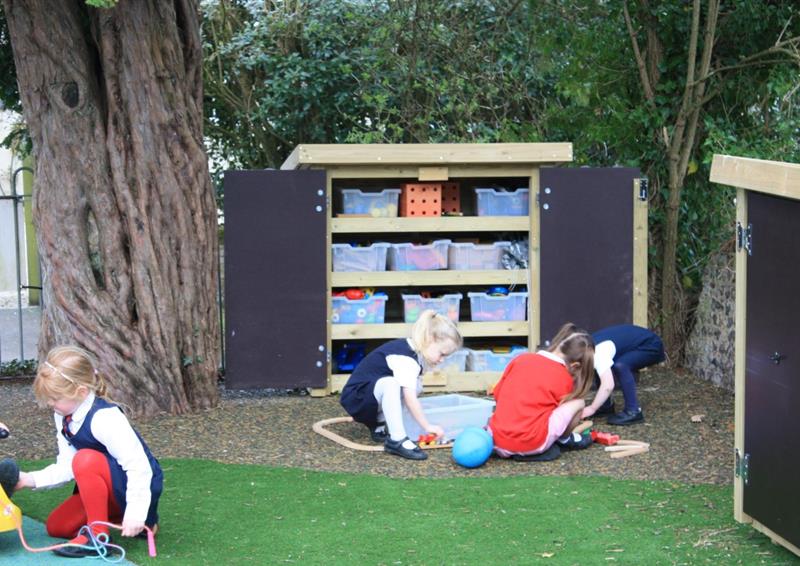 three nursery aged children sit in front of the small storage cupboard that is filled with clear plastic drawers that are organised neatly