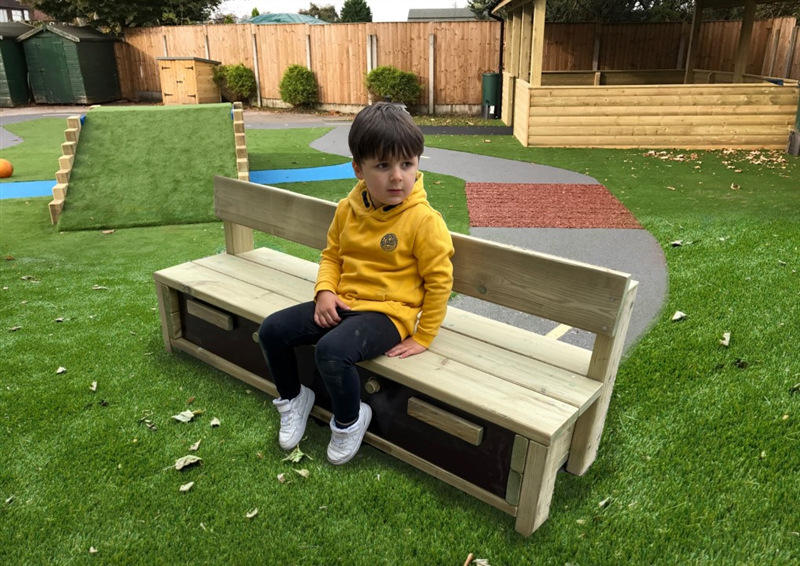 A little boy wearing a yellow jumper and black jeans and white trainers sit on the timber storage bench that has drawers inbuilt for extra storage