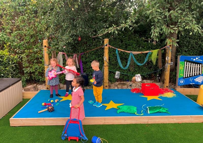 a blue performance stand with den making posts on the back, children play on the stage dancing and singing