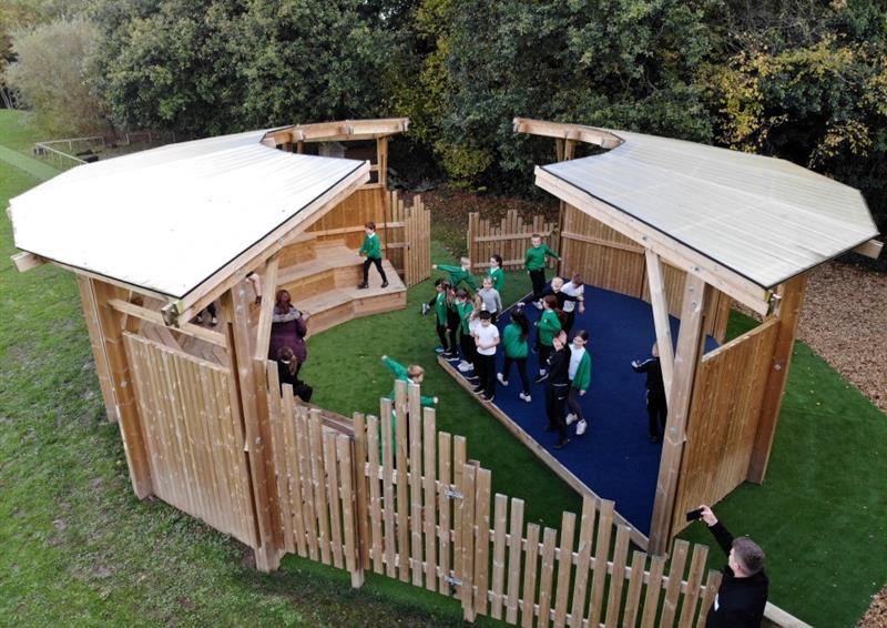 a birdseye view of a timber ampitheatre with ceiling and children gathered within chatting and playing