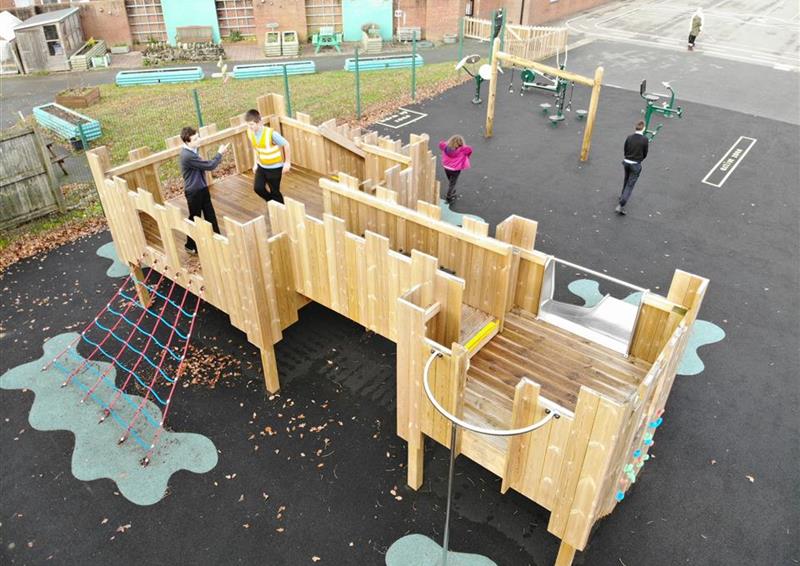 a few children playing on their play castle, there is one young boy stood on top and the rest of the children are stood around.