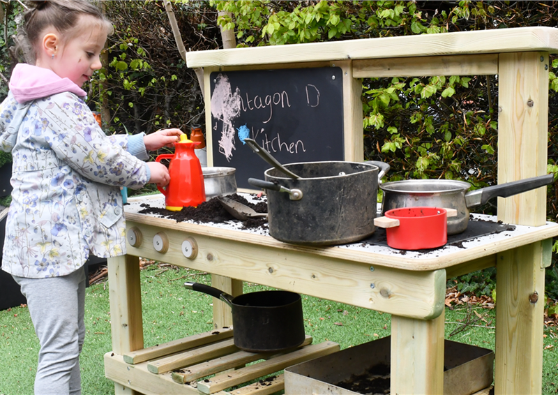 A young girl mixing mud on her mud kitchen in a playground setting