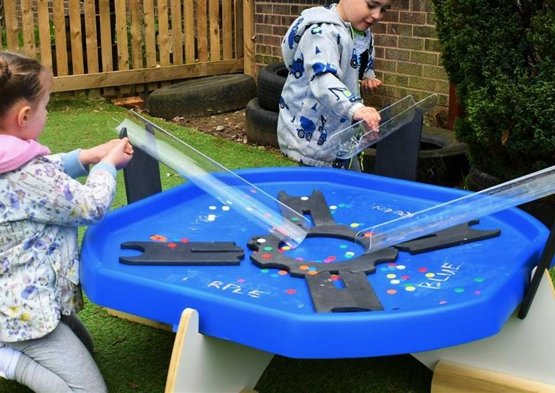 2 young children playing with counters on the tuff spot tray in their playground