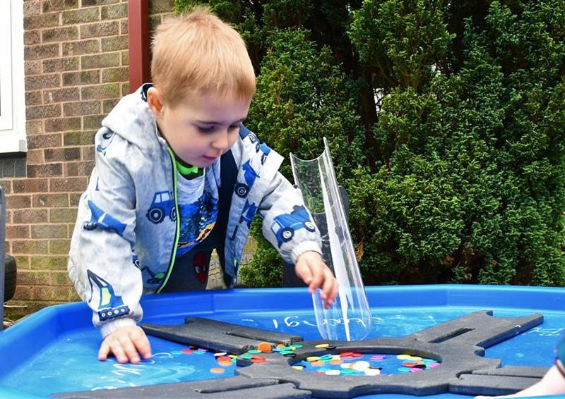 A young boy reaching into the tuff spot tray in his primary school