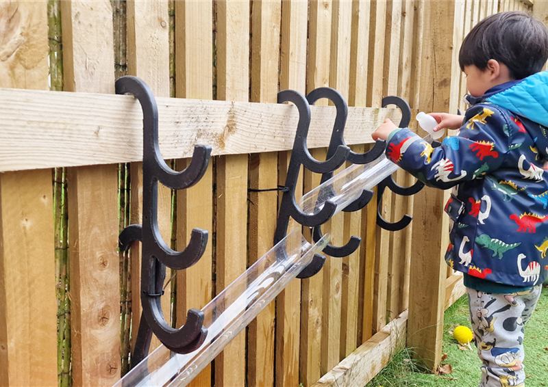 A young boy playing with the water channel hooks that are placed on fencing