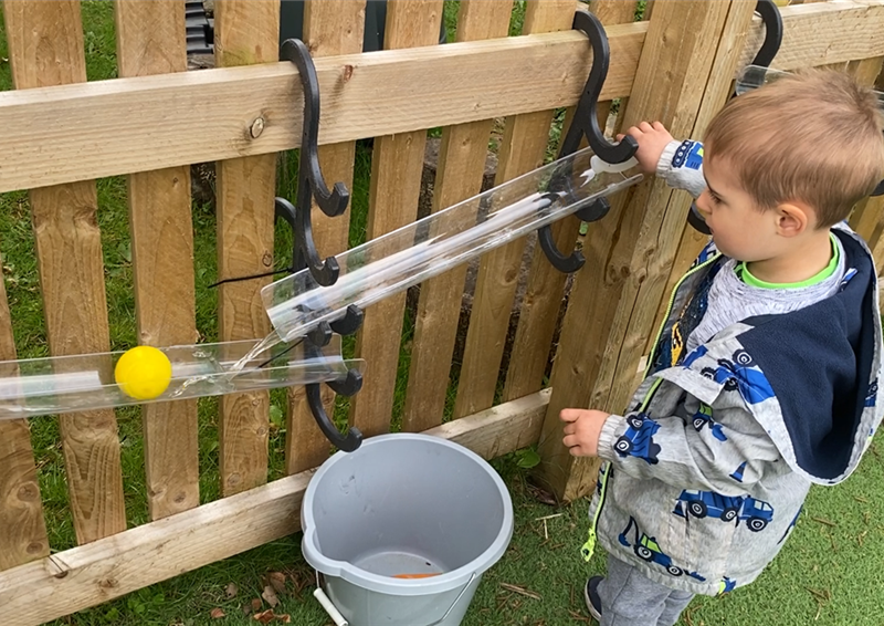 A young boy rolling a ball down the water channels that are connected to fencing