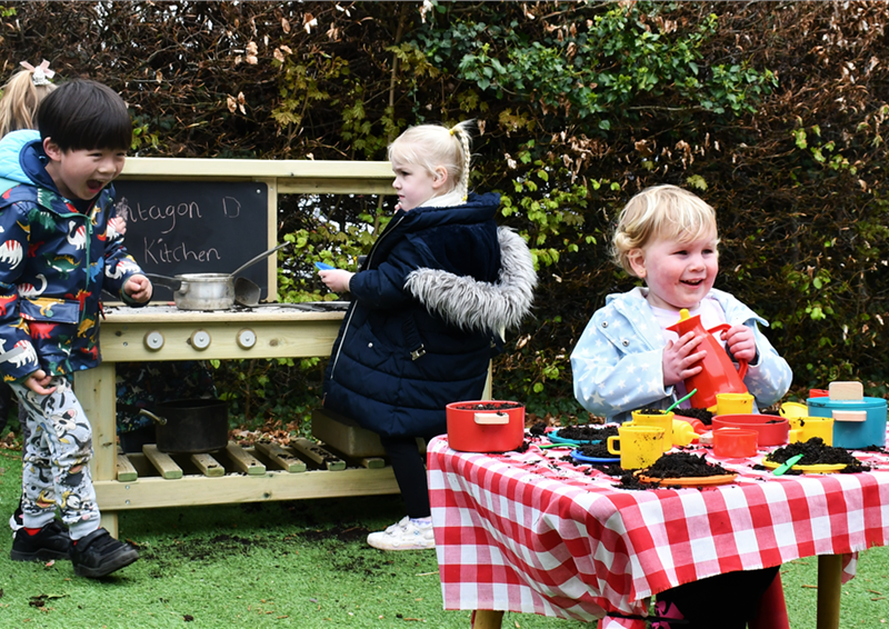 A class of children playing on the mud kitchen in their playground
