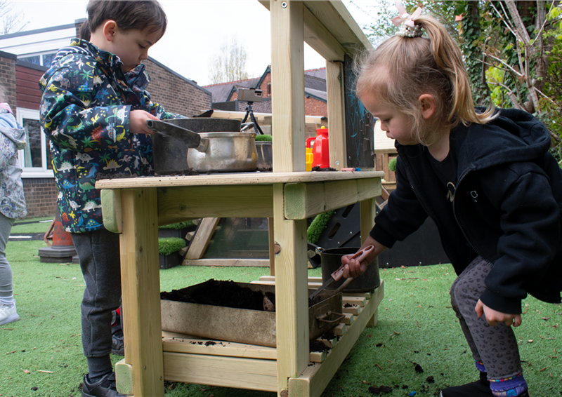 2 young children playing on the mud kitchen for there school