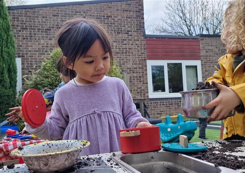2 young children playing with the mud on their mud kitchen