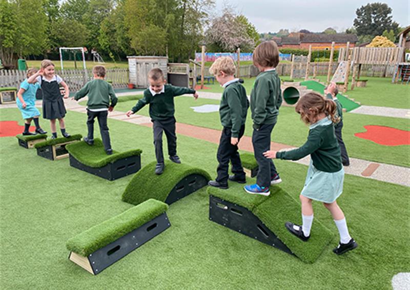School children playing on Get Set, Go! Blocks, which have been placed on an artificial grass surface. The children are in a single file line as they traverse the obstacle course they have created.