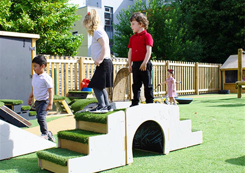 School children playing on Up and Under Blocks. Both the children are stood in the centre of the up and under block, with a variety of Get Set, Go! Blocks surrounding them.