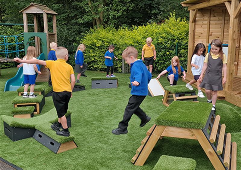 School children playing and climbing on Get Set, Go! Blocks, which have been laid out in a circle format. The children are going around the course in a circle, one behind the other. The course has been set up on artificial grass.