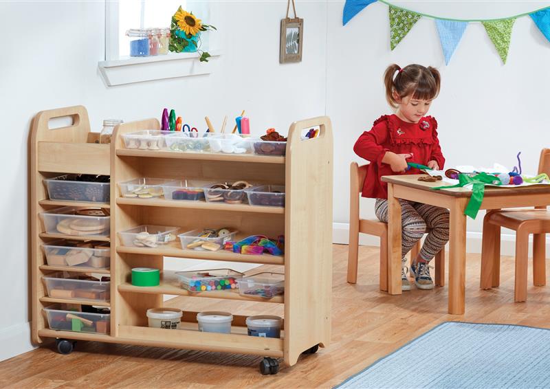 A young girl sitting in front of a Continuous Provision Trolley which is full of arts and crafts supplies