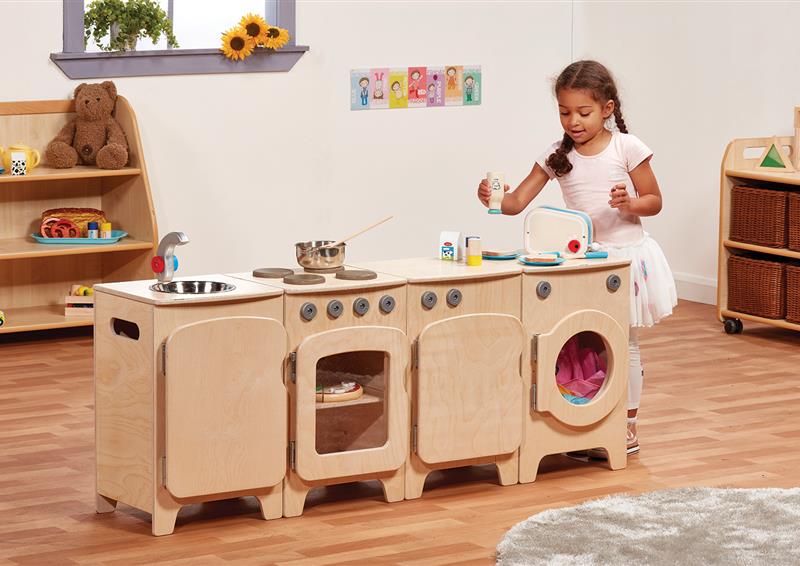 A pre-school aged girl is playing with the Natural Kitchen Set of 4  - Cooker, Sink, Washer, Fridge (H550mm), inside a classroom. 