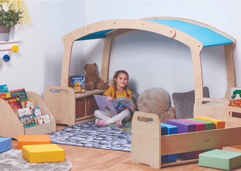 A young girl reading a book in the Mini Rainbow Reading Zone with Baskets, in a classroom