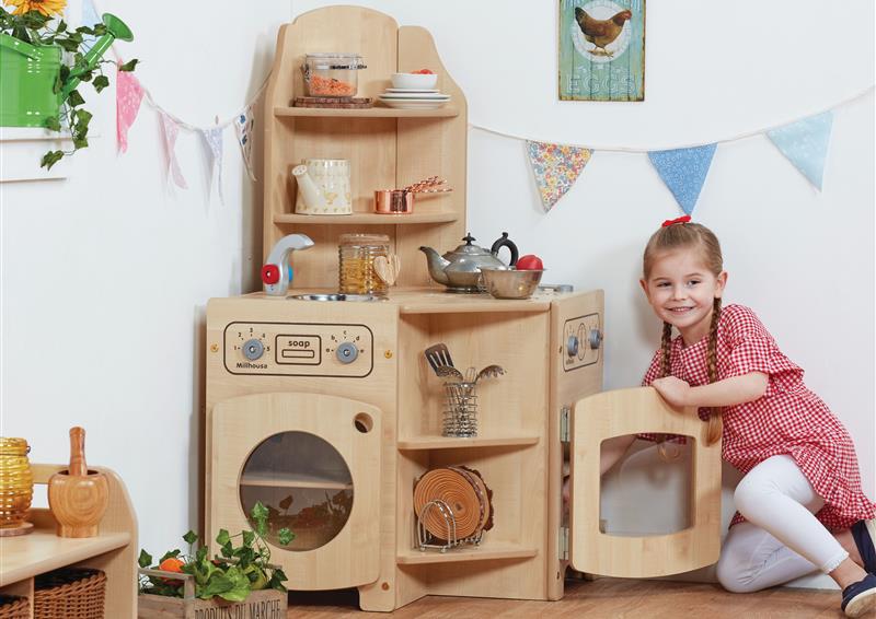A wooden Corner Kitchen with a little girl playing on the floor in a classroom setting