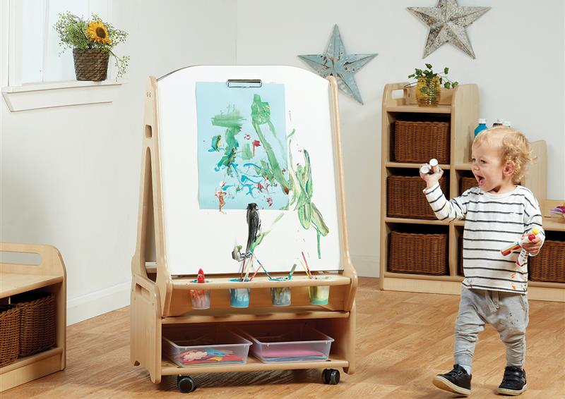 A young boy is painting using the Double-sided 2 Station Whiteboard Easel with Low Storage Trolley