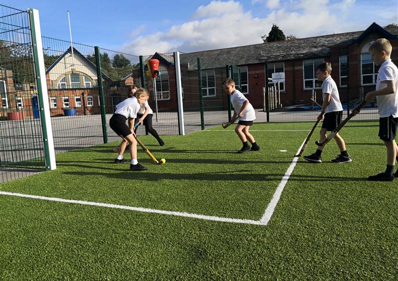 key stage 1 primary school children playing hockey on MUGA pitch