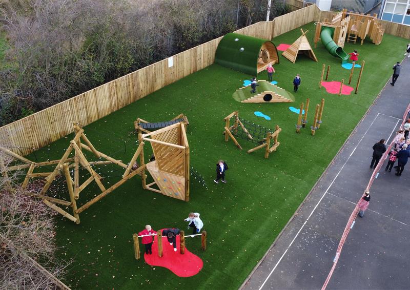 various play equipment across a long artificial grass area in primary school playground