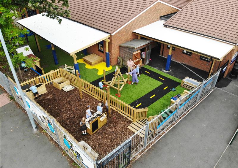 A school playground with canopies, a roadway, and a messy play bark area.