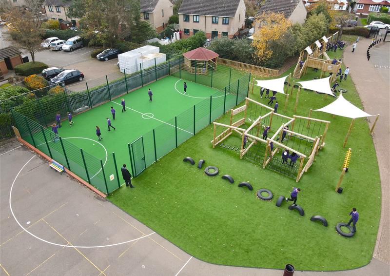 Children playing in a sports pitch area and on a climber next to it. 