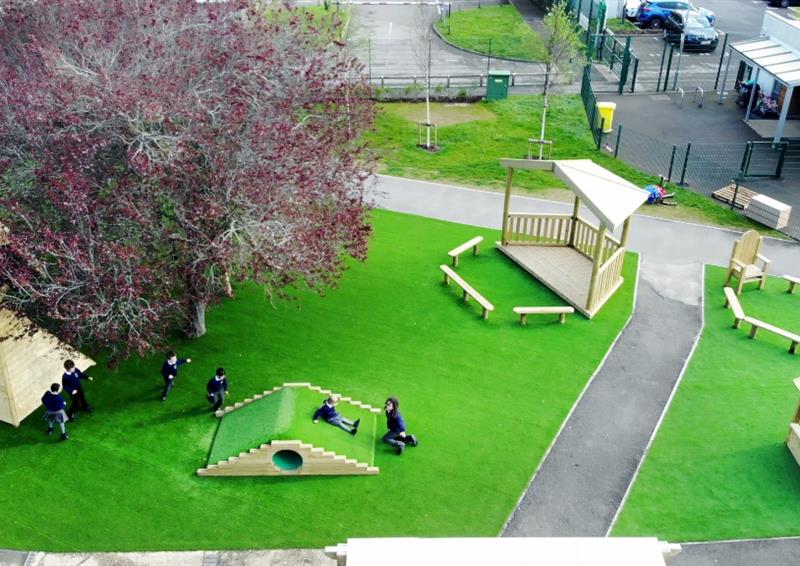 A wide variety of wooden play structures designed and built by Pentagon Play. These wooden structures include a canopy, a playhouse and a wigwam, all installed on artificial grass.